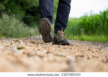 Low angle closeup view of a sole of male hiking shoes walking towards the camera on a gravel country road.