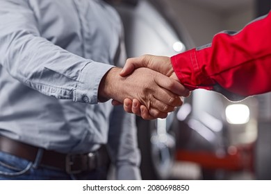 Low angle of crop male car technician and client shaking hands after fixing automobile in modern repair service - Powered by Shutterstock