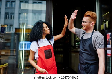 Low angle of delighted multiethnic business partners in casual clothes and apron giving high five to each other while standing on street against entrance of own cafe and rejoicing in success - Powered by Shutterstock