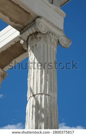 A low angle detailed close up view of an ancient fluted marble column with its spiral volutes capital under a clear blue sky in Athens Greece.