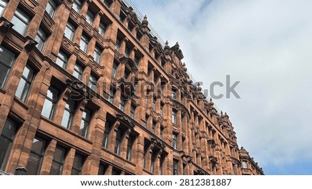 Low angle diagonal view of a historic Victorian sandstone building facade with ornate architectural details and windows against a cloudy sky.