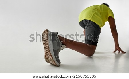 Low angle down back view of athletic black boy waiting on start before run. Male kid wearing sportswear. Modern healthy and sports youngster lifestyle. White background. Studio shoot. Copy space