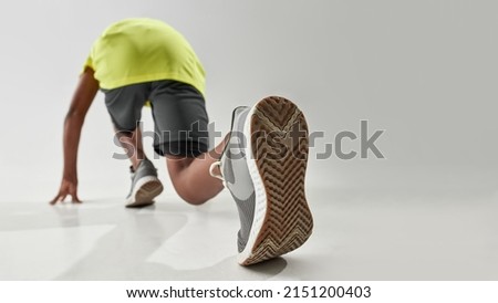 Low angle down back view of athletic black boy waiting on start before run. Male child wearing sportswear. Modern healthy and sports youngster lifestyle. White background. Studio shoot. Copy space