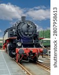 A low angle dramatic frontal view of a classic black steam locomotive with prominent red front beam and headlights standing on a platform track system.