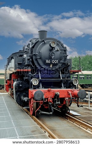 A low angle dramatic frontal view of a classic black steam locomotive with prominent red front beam and headlights standing on a platform track system.