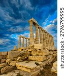 Low angle dramatic view of the ancient stone foundations and pillars of the Poseidon Temple at Cape Sounion under stormy sunset clouds.