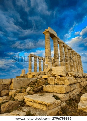 Low angle dramatic view of the ancient stone foundations and pillars of the Poseidon Temple at Cape Sounion under stormy sunset clouds.