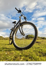 Low angle dramatic view of a mountain bike parked on a green grassy field under a cloudy blue sky 