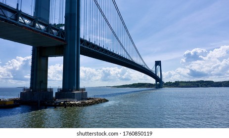 A low angle drone shot, looking up at the superstructure of the Verrazano bridge. The tower on the Brooklyn side is in the forefront of the shot. Shot on a bright and sunny day with clear blue skies