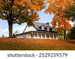 Low angle fall view of patrimonial 19th Century wooden house seen surrounded by trees with colourful foliage in the Cap-Rouge area, Quebec City, Quebec, Canada