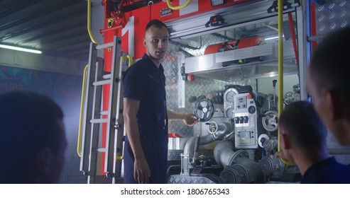 Low angle of fireman showing fire engine mechanism to group of trainees and talking during educational lecture on station - Powered by Shutterstock