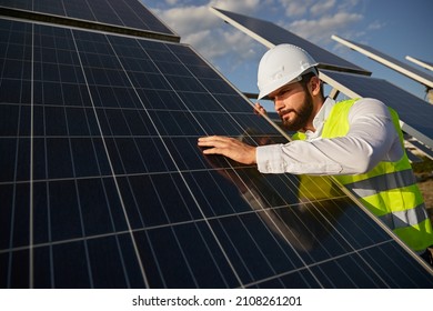Low angle of focused male worker in hardhat checking quality of modern photovoltaic batteries while working in field on sunny day