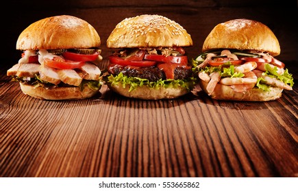 Low angle front view on three delicious chicken, beef and shrimp burgers stuffed with various toppings over wooden table. Includes copy space.