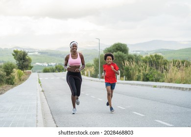 Low angle full body of cheerful active African American mum and son in sportswear jogging while training together in cloudy day