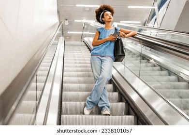 Low angle full length of pensive black woman looking up while standing on escalator in light subway - Powered by Shutterstock