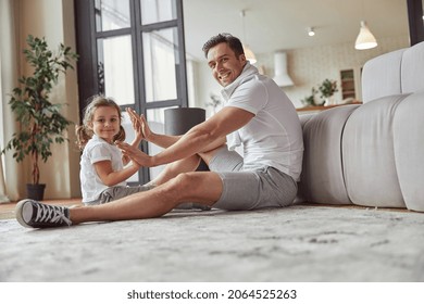 Low Angle Full Length Portrait Of Smiling Girl With Father Sitting On Floor In Living Room And Doing Patty-cake