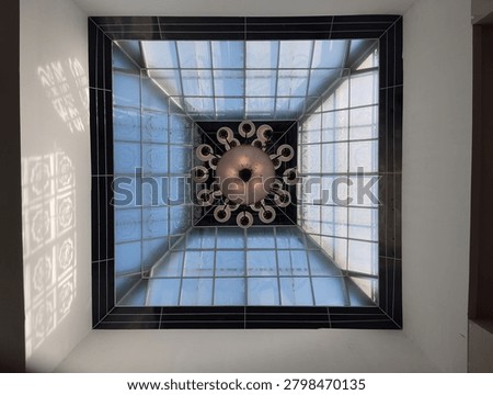 Low angle full shot of a square glass skylight ceiling with a large vintage chandelier hanging in the center, showcasing modern architecture design.