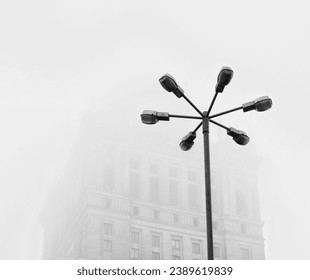 A low angle grayscale shot of a street lamp with multiple lights in front of a building - Powered by Shutterstock