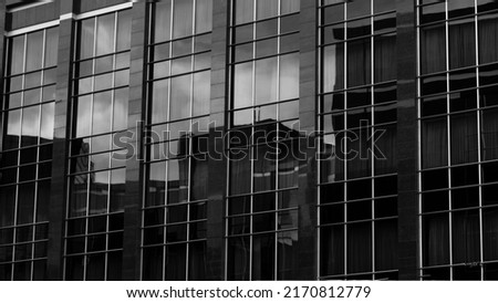 A low angle greyscale of a modern skyscraper under the cloudy sky