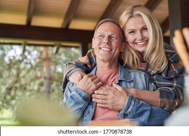 Low angle of happy mature woman embracing husband while relaxing in veranda among green nature