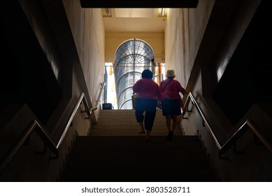 A low angle horizontal shot of two females from behind climbing a dark staircase towards a bright arched doorway in an underpass