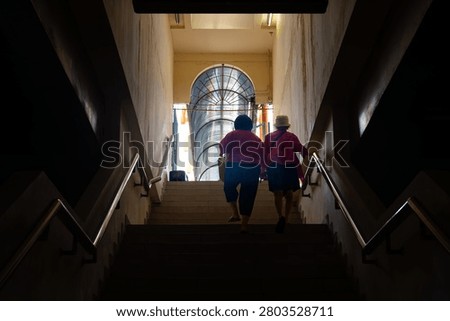 A low angle horizontal shot of two females from behind climbing a dark staircase towards a bright arched doorway in an underpass