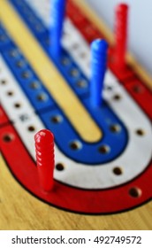 A low angle image of a blue,white, and red cribbage board with blue and red cribbage pegs.