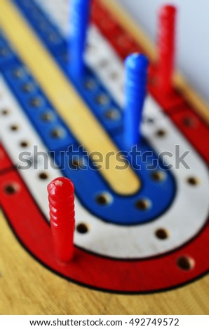 A low angle image of a blue,white, and red cribbage board with blue and red cribbage pegs.