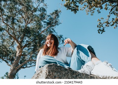 Low Angle Image Of A Body Positive Modern Girl On Jeans And White Shirt With Copy Spac, Trees And Sky Background. Modern Fashion Campaign Ad Concept. Bright Girls World Feminism And Strong Woman