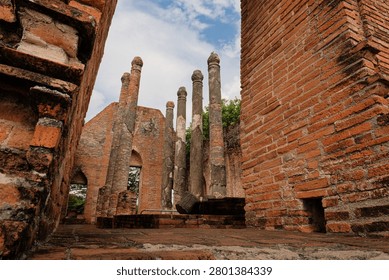 Low angle interior view of ancient red brick walls and weathered pillars inside the ruined assembly hall at Wat Kudi Dao in Ayutthaya, Thailand, looking up towards a cloudy blue sky and green trees
