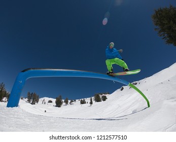 LOW ANGLE, LENS FLARE: Athletic Man On Snowboard Grinds The Rail Set In The Middle Of The Cool Ski Slopes. Extreme Snowboarder Slides Down A Railing On His Board While Riding In Sunny Squaw-Valley.