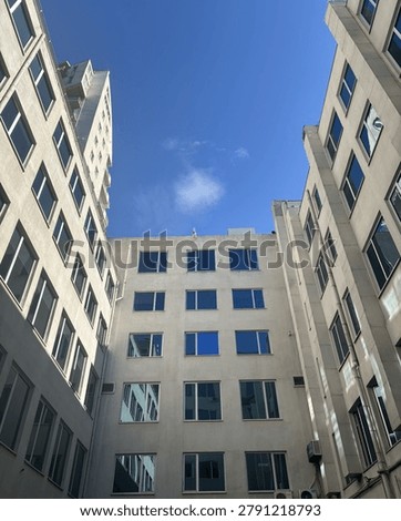 Low angle look up view of a modern white residential or office building courtyard under a bright blue sky, symmetry and urban architecture concept