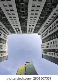 Low angle looking up view of modern apartment buildings with symmetrical geometric architecture design and central copy space sky.