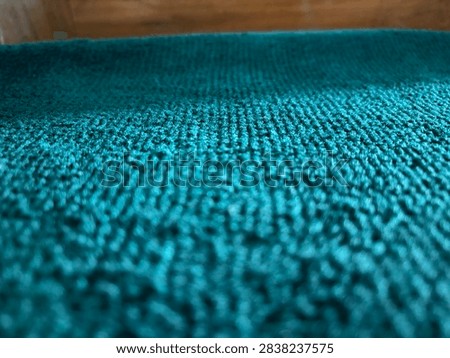 Low angle macro view of teal green carpet fabric texture with soft woven fibers.