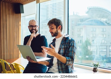 Low angle of male freelancers making investment in successful startup on portable computer and checking earnings while coworking in modern workspace