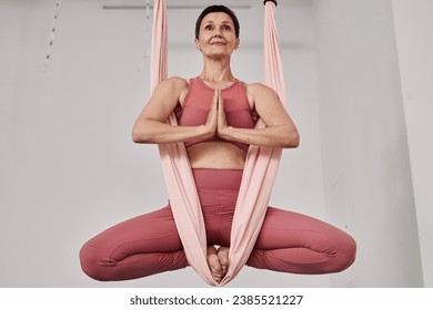 Low angle of mature woman enjoying aerial yoga and meditating in hammock - Powered by Shutterstock