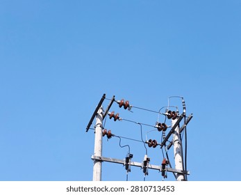 A low angle minimalist shot of double concrete utility poles with electrical ceramic insulators and cables against a clear blue sky. A detailed view of double concrete electricity poles equipped with rows of brown porcelain insulators and fuses under a bright daytime sky.