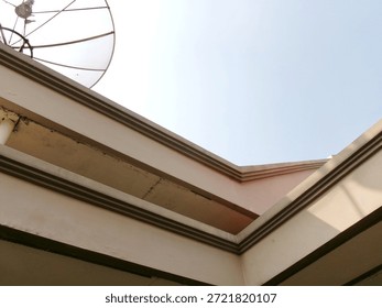 A low angle perspective of a building corner with architectural molding and a satellite dish against a bright overexposed sky.