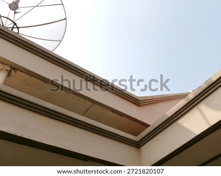 A low angle perspective of a building corner with architectural molding and a satellite dish against a bright overexposed sky.