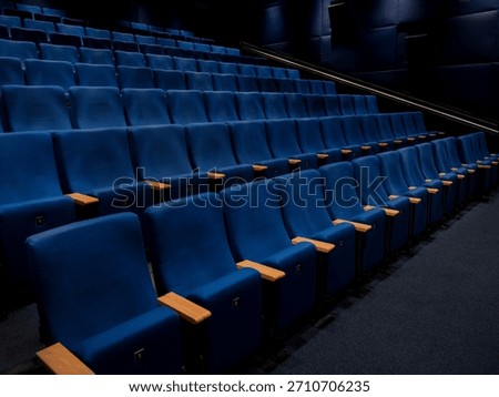 Low angle perspective of cinema seating rows showing blue velvet seats with orange armrests and numbers.