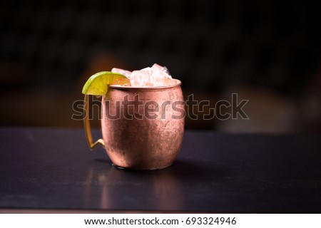 Low angle perspective close up of copper mug with bronze handle filled with acidic Moscow mule alcoholic beverage overflowing with ice cubes and sour lime slice garnish isolated on counter top bar