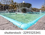 Low angle perspective of corner of pond or reservoir of a quarry fountain, spout with water gushing out, trees and buildings in blurred background, historic center in Guadalajara, Jalisco Mexico