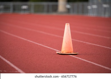 Low Angle Perspective Of Faded Weathered Orange Plastic Traffic Cone On Crushed Red And Maroon Rubber Track And Field Running Surface With White Painted Lane Lines At Exercise Training Fitness Center