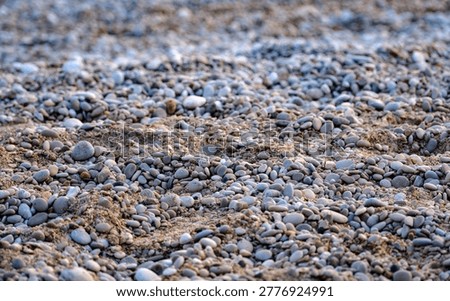 Low angle perspective heavily emphasizing the rugged gritty texture of a natural shoreline composed entirely of dark pebbles and sand.