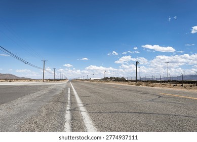 Low angle perspective of a long, straight asphalt road stretching through a vast desert landscape under a blue sky