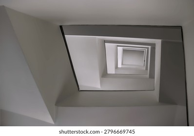 Low angle perspective looking straight up through the square core of a modernist stairwell towards the top landing.