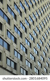 Low angle perspective view of a modernist skyscraper concrete exterior featuring a geometric grid of repeating identical windows with blue glass.