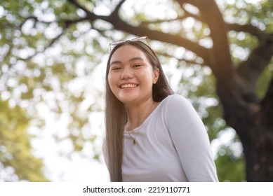 A Low Angle Photo Of An Asian Woman Beaming For The Camera Outside The Park.