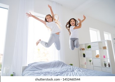 Low angle photo of cheerful kids jumping bed have free time raise hands feel content room indoors apartment