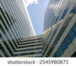 Low angle photo style of geometric pattern and perspective of high-rise buildings with the reflection of white clouds in the glass walls. 